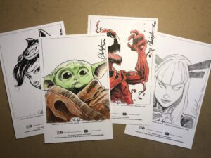 Four different sheets of art paper, each with a different comic book characrter hand-drawn on it.