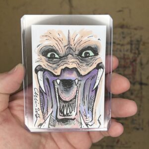Drawing of awide-mouthed, angry-looking Predator figure, with large sharp teeth, on a sketch card.